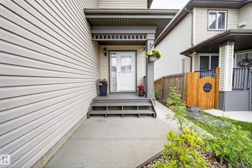 Light-toned horizontal siding with a covered entry, featuring a white paneled door with glass inserts and adjacent sconce lighting - 2518 33A Avenue Nw, Edmonton, AB - Outdoor