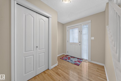 Wood-finish flooring, white bi-fold closet doors, white entry door with sidelight, and a white staircase with balusters - 2518 33A Avenue Nw, Edmonton, AB - Indoor Photo Showing Other Room