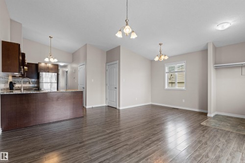Open concept living space featuring wood-finish flooring, a kitchen with dark cabinetry and stainless steel appliances, a breakfast bar with a stone-finish countertop, and a window providing natural light - 10634 155 Street Nw, Edmonton, AB - Indoor Photo Showing Kitchen