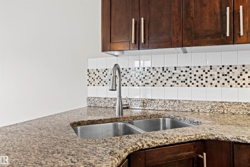 Kitchen sink area featuring a dual stainless steel sink with a gooseneck faucet, granite countertops, and dark wood cabinetry with brushed nickel hardware - 10634 155 Street Nw, Edmonton, AB - Indoor Photo Showing Kitchen With Double Sink