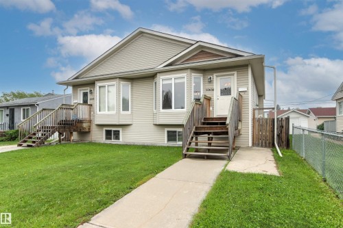 Duplex exterior featuring light-toned siding, two separate front entrances with wooden staircases, and bay windows - 10634 155 Street Nw, Edmonton, AB - Outdoor With Facade