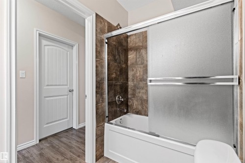 Tub and shower combination featuring brown tile surround and frosted glass sliding doors - 10634 155 Street Nw, Edmonton, AB - Indoor
