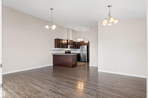 Open-concept living space featuring wood-finish flooring, a kitchen island with stone countertop, dark wood cabinetry, stainless steel appliances, and a mosaic tile backsplash - 10634 155 Street Nw, Edmonton, AB - Indoor Photo Showing Kitchen