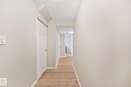 Hallway with wood-finish flooring, light neutral wall paint, white baseboards, and a paneled interior door with a brass-finish knob - 3769 21 Street Nw, Edmonton, AB - Indoor Photo Showing Other Room