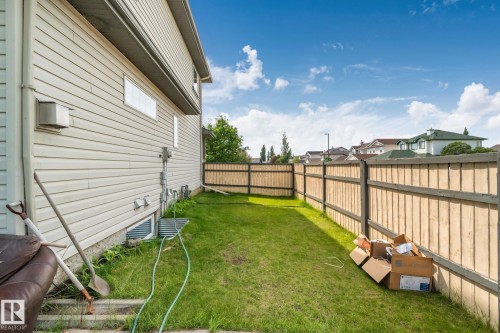Grassed side yard featuring a new privacy fence, beige vinyl siding, and a basement window well - 3769 21 Street Nw, Edmonton, AB - Outdoor With Exterior