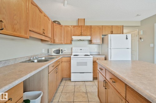 Kitchen featuring wood-finish cabinetry, a double basin stainless steel sink, tile flooring, a white electric range, and a white refrigerator - 3769 21 Street Nw, Edmonton, AB - Indoor Photo Showing Kitchen With Double Sink