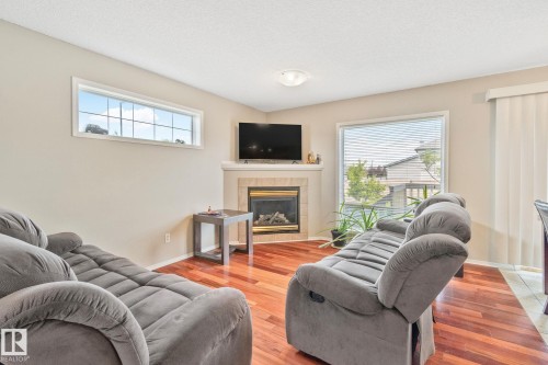 Living area featuring rich wood-finish flooring and a corner fireplace with a stone surround - 3769 21 Street Nw, Edmonton, AB - Indoor Photo Showing Living Room With Fireplace