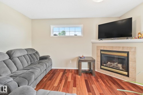 Warm interior featuring wood-finish flooring, a contemporary fireplace with a tile surround and mantel, and an overhead lighting fixture - 3769 21 Street Nw, Edmonton, AB - Indoor Photo Showing Living Room With Fireplace