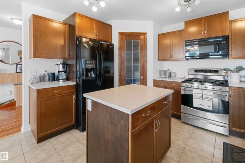 Kitchen featuring wood cabinetry, stainless steel range, black refrigerator, kitchen island with countertop, and tile flooring - 6515 37 Avenue, Beaumont, AB - Indoor Photo Showing Kitchen
