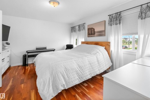 Hardwood flooring, multiple windows with blinds, wood-finish bed frame, ceiling-mounted light fixture, white walls - 6515 37 Avenue, Beaumont, AB - Indoor Photo Showing Bedroom