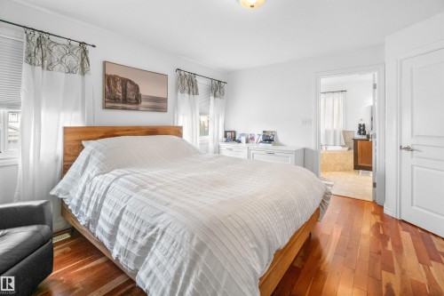 Hardwood-style flooring, white walls, built-in light fixture, white trim windows, and a bathroom entry - 6515 37 Avenue, Beaumont, AB - Indoor Photo Showing Bedroom