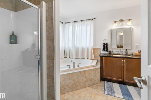 Glass-enclosed shower, corner soaking tub with tiled surround, single vanity with wood-finish cabinetry, dark countertop, and an illuminated mirror - 6515 37 Avenue, Beaumont, AB - Indoor Photo Showing Bathroom