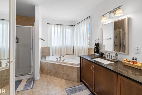 Built-in corner bathtub, glass-enclosed shower, wood-finish vanity with an integrated sink, dark countertop, and tiled flooring - 6515 37 Avenue, Beaumont, AB - Indoor Photo Showing Bathroom