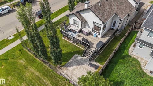 Rear exterior showcasing an elevated deck with black railing, a lower-level wood deck, and a manicured lawn - 6515 37 Avenue, Beaumont, AB - Outdoor