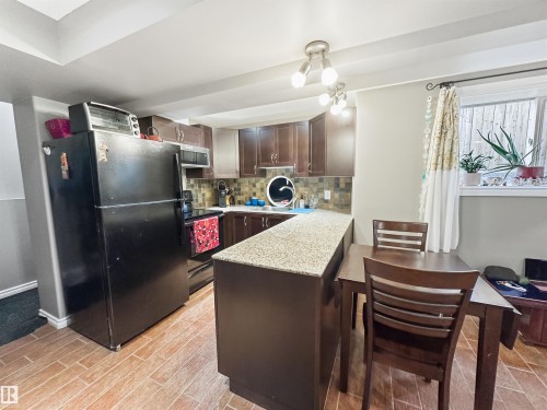 Kitchen featuring wood-finish flooring, dark wood cabinetry, a light-toned countertop, and a tiled backsplash - 6515 37 Avenue, Beaumont, AB - Indoor Photo Showing Kitchen