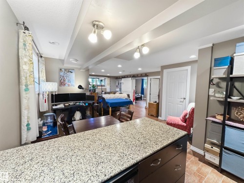 Expansive open-concept room featuring a speckled countertop island, dark wood-finish cabinetry with silver hardware, recessed ceiling lighting, and track lighting - 6515 37 Avenue, Beaumont, AB - Indoor