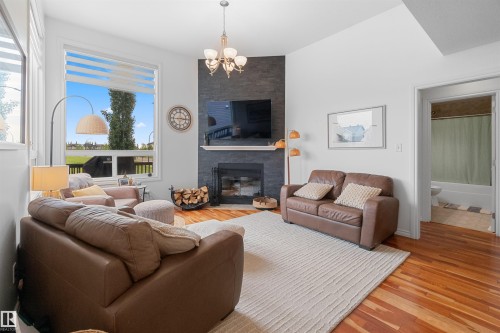 Hardwood flooring, corner fireplace with stone surround, large picture window, and chandelier lighting - 6515 37 Avenue, Beaumont, AB - Indoor Photo Showing Living Room With Fireplace