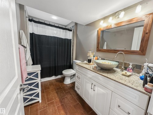 Full bathroom featuring wood-finish flooring, a vanity with a light-toned countertop, a vessel sink, and a framed mirror - 6515 37 Avenue, Beaumont, AB - Indoor Photo Showing Bathroom