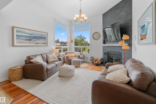 Hardwood flooring, fireplace with stone surround, white mantle, and large windows - 6515 37 Avenue, Beaumont, AB - Indoor Photo Showing Living Room With Fireplace