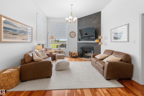 Vaulted ceiling, stone-clad fireplace, hardwood flooring, large windows, and an overhead chandelier - 6515 37 Avenue, Beaumont, AB - Indoor Photo Showing Living Room With Fireplace