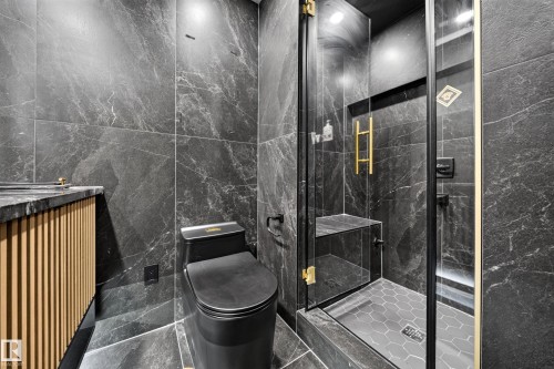 Floor-to-ceiling tile, walk-in shower with built-in bench, black toilet, gold-tone fixtures, and a vanity with a fluted wood-finish front - 4301 38 St, Beaumont, AB - Indoor Photo Showing Bedroom