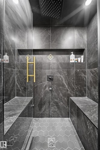 Spa-inspired shower enclosure featuring large-format dark stone tile walls, a rainfall showerhead, dual built-in benches with matching stone surfaces, hexagonal tile flooring, and brushed brass hardware accents - 4301 38 St, Beaumont, AB - Indoor Photo Showing Bedroom