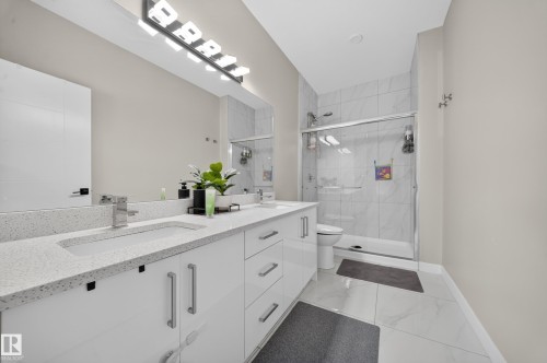 Dual vanity with integrated sinks and white cabinetry, stone-finish countertops, and a large mirror - 4301 38 St, Beaumont, AB - Indoor Photo Showing Bathroom