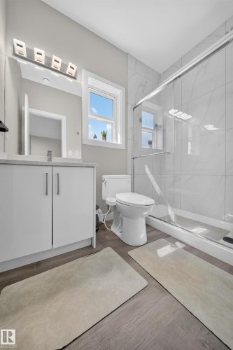 Modern primary bathroom featuring dual vanity with white cabinetry and integrated sink, frameless glass shower enclosure, subway tile surround, recessed ceiling lighting, and wood-finish flooring throughout - 4301 38 St, Beaumont, AB - Indoor Photo Showing Bathroom