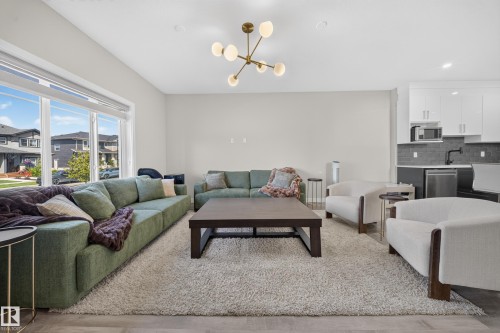 Spacious open-concept living area featuring a green upholstered sectional sofa, dark wood coffee table, neutral area rug, and a modern brass sputnik ceiling fixture - 4301 38 St, Beaumont, AB - Indoor Photo Showing Living Room