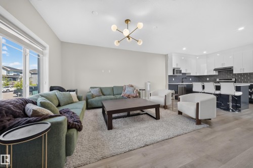 Open-concept living area featuring a modern chandelier, large windows, and light wood-finish flooring - 4301 38 St, Beaumont, AB - Indoor Photo Showing Living Room