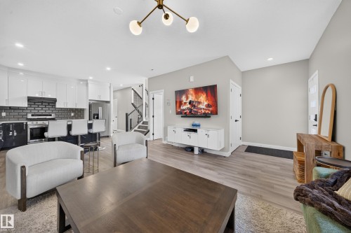 Open-concept living space featuring warm wood-finish flooring, a substantial dining table, and a gas fireplace with built-in cabinetry - 4301 38 St, Beaumont, AB - Indoor Photo Showing Other Room
