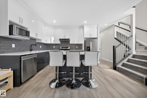 Kitchen featuring white upper cabinetry, dark lower cabinetry, stainless steel appliances, and a dark subway tile backsplash - 4301 38 St, Beaumont, AB - Indoor Photo Showing Kitchen With Upgraded Kitchen