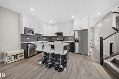 Kitchen featuring wood-finish flooring, white cabinetry, dark gray subway tile backsplash, and stainless steel appliances - 4301 38 St, Beaumont, AB - Indoor Photo Showing Kitchen With Upgraded Kitchen