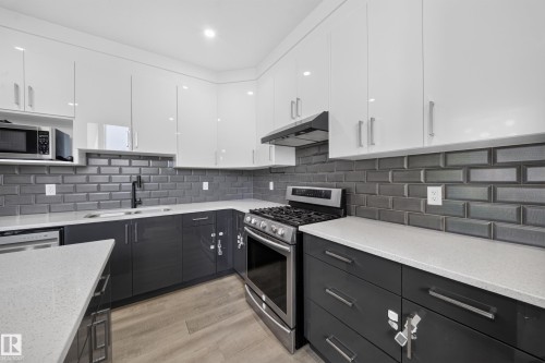 Two-tone cabinetry with white upper cabinets and dark lower cabinets, gray subway tile backsplash, light-toned countertops, and wood-finish flooring - 4301 38 St, Beaumont, AB - Indoor Photo Showing Kitchen With Upgraded Kitchen