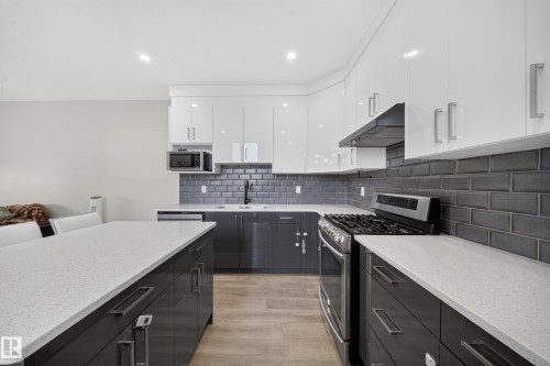 Contemporary kitchen featuring two-tone cabinetry, light-toned countertops, subway tile backsplash, stainless steel appliances, and wood-finish flooring - 4301 38 St, Beaumont, AB - Indoor Photo Showing Kitchen With Upgraded Kitchen