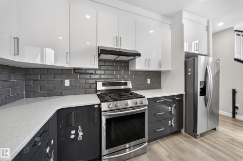 Kitchen featuring stainless steel appliances, white upper cabinetry, dark lower cabinetry, light-toned countertops, and a dark subway tile backsplash - 4301 38 St, Beaumont, AB - Indoor Photo Showing Kitchen With Upgraded Kitchen