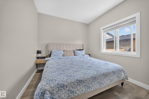 Bright secondary bedroom featuring a vertical shiplap accent headboard, wood-finish flooring, soft neutral wall tones, and abundant natural light from a large multi-pane window framing scenic mountain vistas - 4301 38 St, Beaumont, AB - Indoor Photo Showing Bedroom