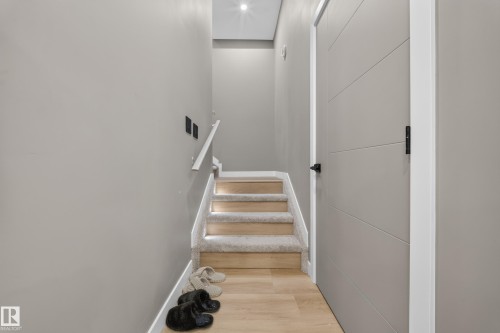 Staircase with carpeted treads and wood-finish risers, integrated step lighting, a white handrail, and a contemporary panel door with matte black hardware - 4301 38 St, Beaumont, AB - Indoor Photo Showing Other Room