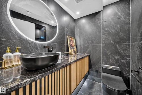 Backlit oval mirror, black vessel sink, matte black faucet, dark stone-finish countertops, wood-slat vanity with integrated lighting - 4301 38 St, Beaumont, AB - Indoor Photo Showing Bedroom