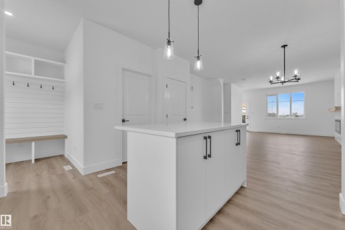Kitchen island with a light-toned countertop, wood-finish flooring, two pendant lights, and built-in entry bench with shelving - 82 Patriot Way, Spruce Grove, AB - Indoor