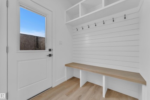 Built-in storage bench with wood-finish top, shiplap wall paneling, integrated coat hooks, and overhead shelving - 82 Patriot Way, Spruce Grove, AB - Indoor Photo Showing Other Room