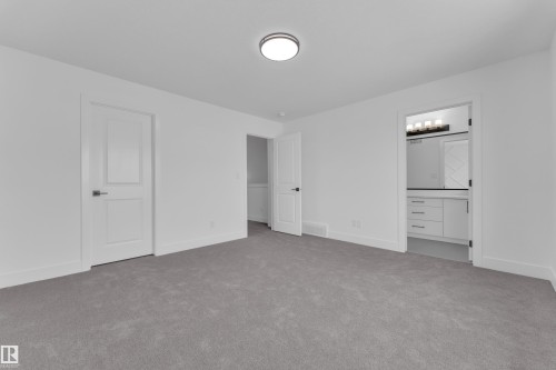 Plush gray carpeting, white walls, modern flush mount ceiling light, white paneled doors with dark hardware, and visible vanity with white cabinetry - 82 Patriot Way, Spruce Grove, AB - Indoor Photo Showing Other Room
