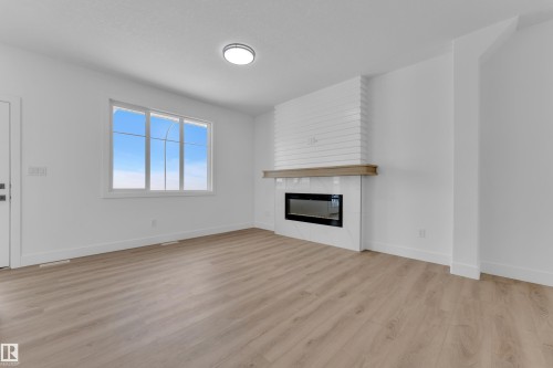 Spacious room featuring wood-finish flooring, a contemporary fireplace with a decorative mantel, and a multi-pane window - 82 Patriot Way, Spruce Grove, AB - Indoor Photo Showing Living Room With Fireplace