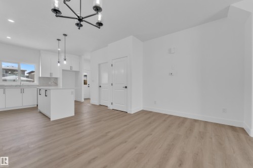 Open-concept living area featuring wood-finish flooring, a contemporary chandelier, white kitchen cabinetry, a kitchen island with pendant lighting, and crisp white walls - 82 Patriot Way, Spruce Grove, AB - Indoor Photo Showing Kitchen