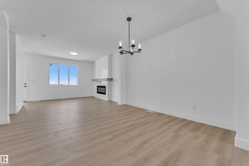 Spacious room with wood-finish flooring, a white brick-finish fireplace, wood mantel, and a multi-pane window - 82 Patriot Way, Spruce Grove, AB - Indoor With Fireplace