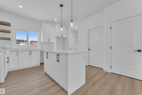 White shaker cabinetry with matte black hardware, large center island, wood-finish flooring, recessed lighting, and a window above the sink - 82 Patriot Way, Spruce Grove, AB - Indoor Photo Showing Kitchen