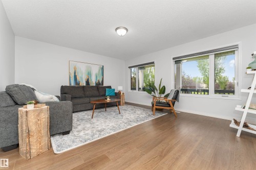 Vinyl flooring throughout, white painted walls, and white trim with large triple pane windows with a view of the park. - 4121 Tompkins Way Nw, Edmonton, AB - Indoor Photo Showing Living Room