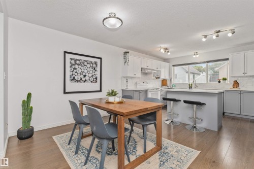 Wood-finish flooring, white walls, kitchen island with seating, white cabinetry, and a tile backsplash - 4121 Tompkins Way Nw, Edmonton, AB - Indoor Photo Showing Other Room