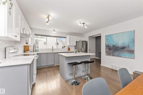 Kitchen featuring Vinyl plank flooring, white cabinetry, gray lower cabinetry, white quartz countertops, and a center island - 4121 Tompkins Way Nw, Edmonton, AB - Indoor Photo Showing Kitchen