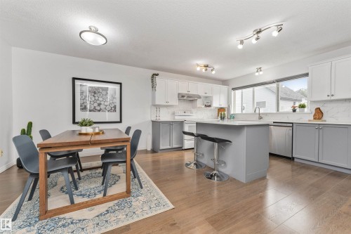 Open-concept living area featuring Vinyl plank flooring, a kitchen with stainless steel appliances, a large center island with countertop seating, quartz counters with white and gray cabinetry, and a dining area - 4121 Tompkins Way Nw, Edmonton, AB - Indoor